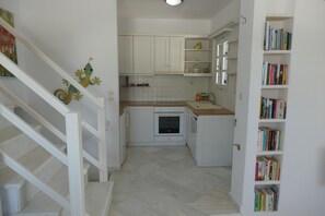 A kitchen with white cabinets, a built-in oven, and a bookshelf filled with books. - Charming Naxos Villa, Ocean Views, Modern Comfort, Tranquil Escape (Naxos)