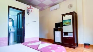 Una habitación de hotel con cama, escritorio, silla, armario y ventilador de techo.