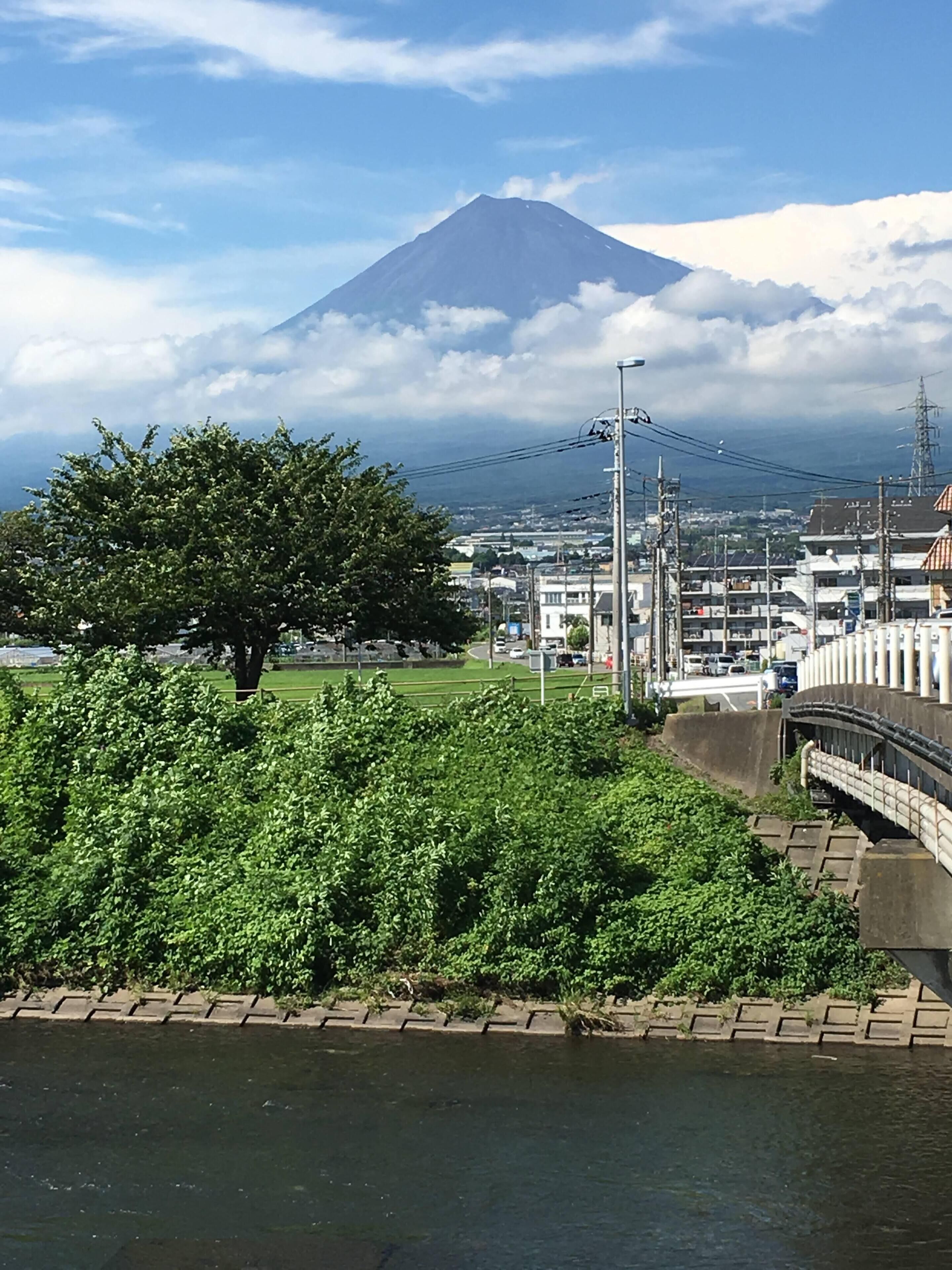 A river with a bridge, a tree-lined area, and a mountain in the background.