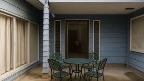 A covered patio with a round table and four chairs, a door leading to an interior space, and a window with blinds.
