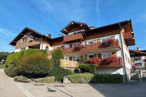 Un chalet à plusieurs étages doté de balcons en bois, d’un jardin bien entretenu et surplombant un ciel dégagé.