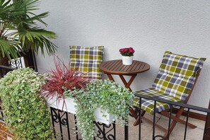 Ein Balkon mit einem kleinen runden Tisch, zwei karierten Stühlen und Topfpflanzen.