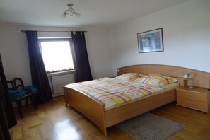Ein Schlafzimmer mit einem hölzernen Bett, einem Nachttisch, einem Schreibtisch und einem Fenster mit Vorhängen.