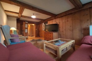 Ein gemütliches Zimmer mit Holzwänden, einem Fernseher auf einem Holzschrank, einer Couch, einem Sessel und einem Couchtisch.