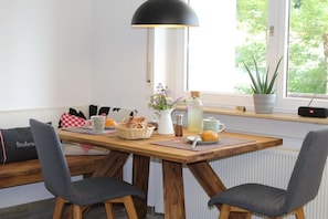 A dining area with a wooden table, two chairs, a lamp, and a window with a view of greenery. - Holiday apartment with 1 bedroom (Todtnauberg \/ Schwarzwald)