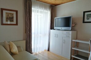 Ein Zimmer mit einer Couch, einem Fernseher auf einem Schrank, einer Heizung und einem Fenster mit Vorhängen.