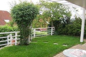 Ein Garten mit weißem Zaun, einer Pergola und einem Glastisch mit rosa Tischdecke.