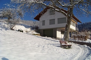 Ein zweistöckiges Haus mit großer Garage, umgeben von schneebedecktem Gelände und Bäumen.