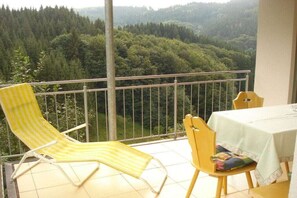 Ein Balkon mit einem gelb gestreiften Stuhl, einem Holzstuhl und einem Tisch mit weißem Tischläufer.