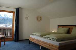 A bedroom with a wooden bed, a view of mountains through a balcony, and a small table. - Holiday home with 3 bedrooms (Oberstdorf \/ Tiefenbach)