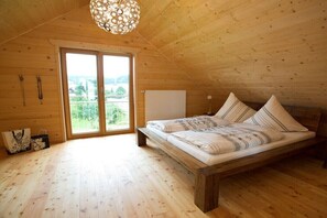 Ein Zimmer mit Holzwänden, einem Bett, einem großen Fenster und einer Pendelleuchte.