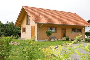 Ein zweistöckiges Haus mit Satteldach, einer Veranda und einem kleinen Garten mit Bank und Blumentöpfen.