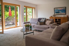 Ein Wohnzimmer mit einer Couch, einem Couchtisch mit Blumen und einer Flasche, einem Holzkabinett und einem Gemälde an der Wand.