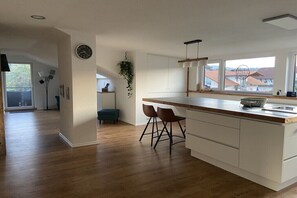 Eine moderne Küche mit einer großen Kochinsel, Holzboden und Blick auf Häuser durch die Fenster.