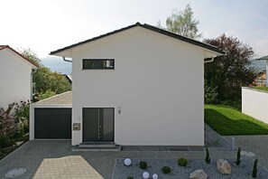Ein modernes, zweistöckiges Haus mit Garage, einem kleinen Vorgarten und blauem Himmel.