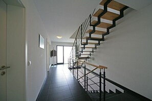 Eine moderne Treppe mit Holzboden und Metallgeländern, die zu einem hellen Raum mit einer Tür links führt.