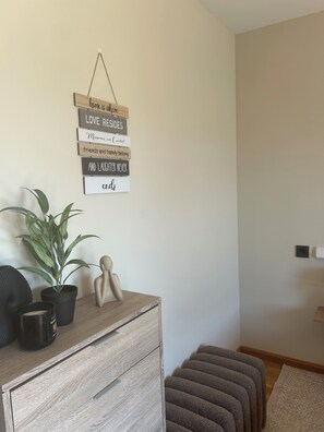 A room with a wooden dresser, a potted plant, a wall-mounted sign with motivational phrases, and a staircase.