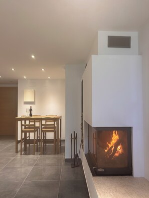 A modern living room with a fireplace, a dining table with chairs, and recessed ceiling lights.