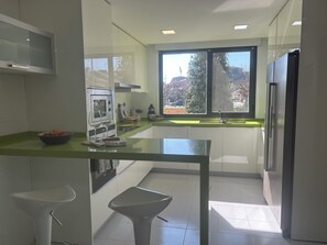 A modern kitchen with a glass table, stainless steel appliances, and a view of the outside.