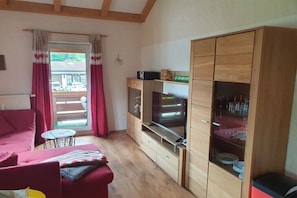 A room with a red sofa, wooden cabinets, a television, and a small table. - Holiday apartment in Oberstdorf with Wi-Fi (Oberstdorf)