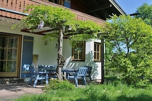 Ein Gebäude mit überdachter Terrasse, Sitzgelegenheiten im Freien und einem Baum.