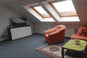 A room with a sloped ceiling, skylights, a sofa, a small table with a lamp, a cabinet, and a television. - Holiday apartment with 2 bedrooms (Zimmern ob Rottweil, OT Horgen)
