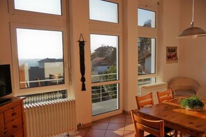 A dining area with a wooden table and chairs, large windows with views of buildings, a radiator, and a hanging light fixture. - "A" in the house with panoramic view (Ettenheim)