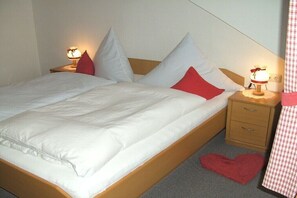 Ein Bett mit weißer Bettwäsche, zwei Nachttische mit Lampen, ein Holz-Kopfteil und ein roher Teppich in Herzform auf dem Boden.