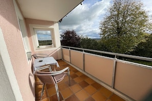 A balcony with a table and chairs, a window with a view of trees and hills, and a tiled floor. - Dippold holiday farm - near 95326 Kulmbach (Ködnitz)