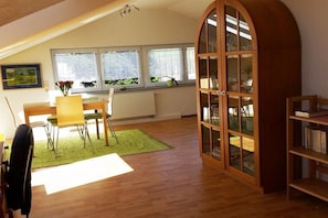 A room with a dining table, chairs, a bookshelf, a large arched window, and a radiator. - Holiday apartment with 2 bedrooms (Wangen)