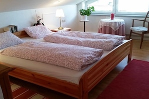 A wooden bed with floral bedding, a bedside lamp, a small table with a plant, and a chair. - Holiday apartment with 2 bedrooms (Wangen)