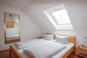 Ein Schlafzimmer mit Dachfenster, einem Bett mit weißen Leinen, einem Holz-Kopfende, einem Nachttisch mit Lampe und einem Spiegel an der Wand.