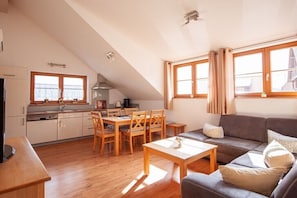 Eine moderne Küche mit Holzschränken, einem Esstisch mit Stühlen, einer Couch und großen Fenstern mit Vorhängen.