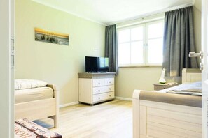Ein Zimmer mit einem Bett, einem Fernseher auf einer Kommode, einem Fenster mit Vorhängen und einem Gemälde an der Wand.