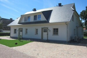 Ein zweistöckiges Haus mit geneigtem Dach, einer Veranda und einem gepflasterten Einfahrt.