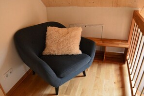 Ein dunkelblauer Sessel mit einem flauschigen beigen Kissen in einem Raum mit Holzboden und Holzzahl.