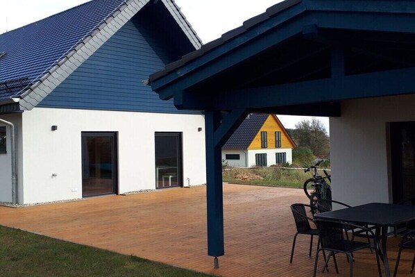 Ein modernes Gebäude mit blauem Dach, einer Holzterrasse und einer überdachten Patio mit Tisch und Stühlen.