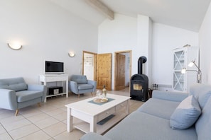 Ein Wohnzimmer mit einer Couch, zwei Sesseln, einem Fernseher, einem Kamin und einem Schrank.