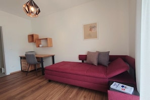 Ein kleiner Raum mit einem roten Sofa, einem Holztisch, einem Stuhl und einer Pendelleuchte.