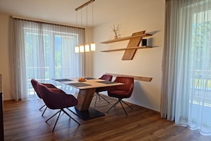 Ein moderner Essbereich mit Holztisch, roten Stühlen, Pendelleuchten und Blick durch große Fenster.