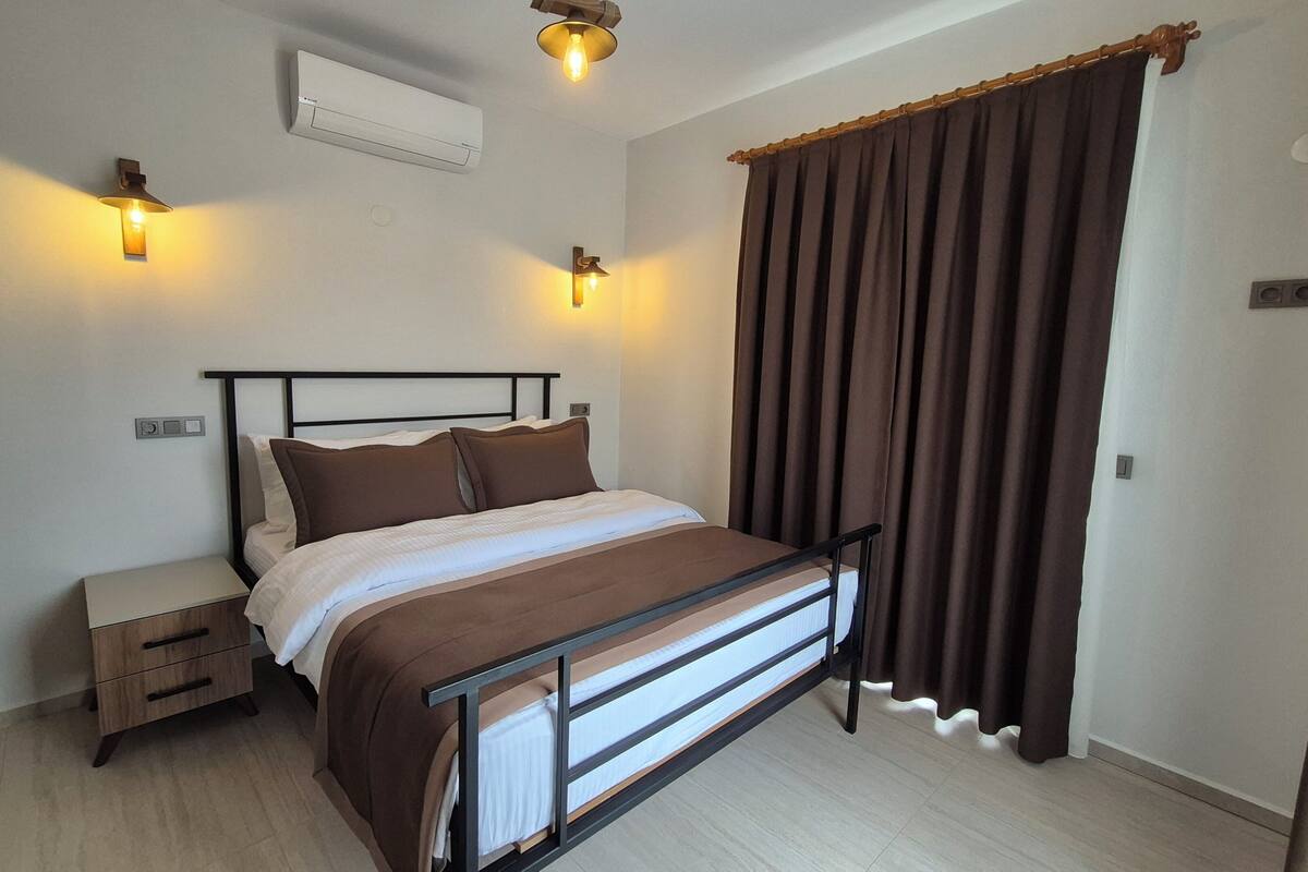 A bedroom with a bed, bedside tables, an air conditioning unit, and a curtain.
