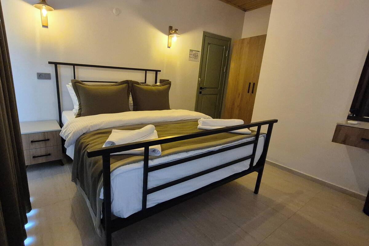 A single bed with a metal frame, a wooden door, a small bedside table, and two wall-mounted light fixtures.