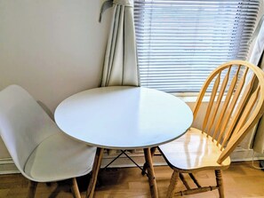 Ein runder Tisch mit zwei Stühlen, ein Fenster mit Jalousien und einem Vorhang.