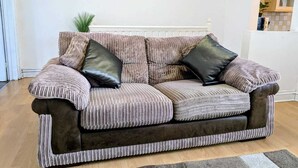 A striped sofa with two black cushions, a framed artwork above, and a kitchen visible through an archway. - Contractor Business Family Stay Near Southampton Airport 1BR (Eastleigh)