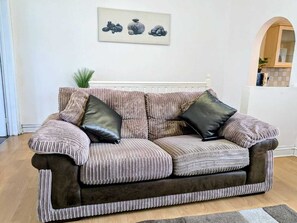 Ein gestreiftes Sofa mit zwei schwarzen Kissen, ein gerahmtes Kunstwerk darüber und ein durch einen Bogen sichtbarer Küchenbereich.