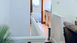 A narrow hallway leading to a kitchen with a washing machine, a window, and a white railing. - Contractor Business Family Stay Near Southampton Airport 1BR (Eastleigh)