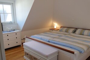 Ein Schlafzimmer mit Bett, Nachttisch, Lampe, Fenster und Kommode.