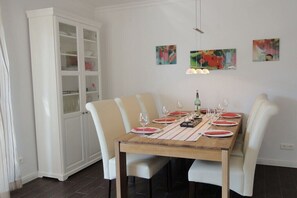 Ein Essbereich mit einem Holztisch, gedeckt für sechs Personen, weißen Stühlen und einem weißen Schrank mit Glastüren.