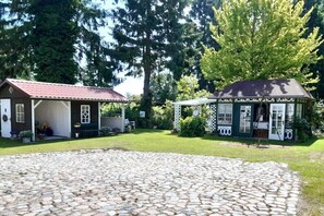 Una baita rustica con un patio in pietra, un piccolo deposito e un gazebo immersi nel verde.