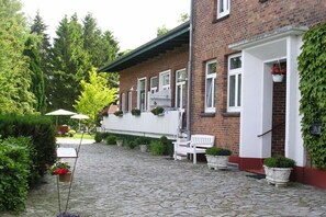 A brick building with a white porch, potted plants, and a stone pathway. - VI "Refuge" - House Avalon (Grube)